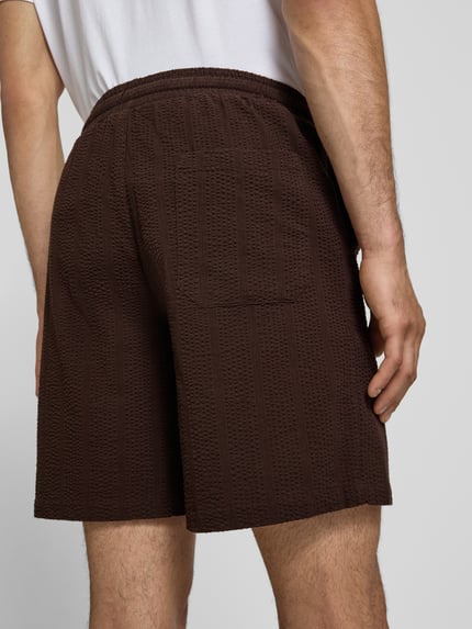 Männermodel trägt Loose Fit Shorts aus reiner Baumwolle Modell 'CRUZ' von Only & Sons in Optik: Unifarben, Materialverarbeitung: Seersucker, Bundabschluss: elastisch, Gesäßtasche sichtbar, Ganzkörperansicht Rückansicht.