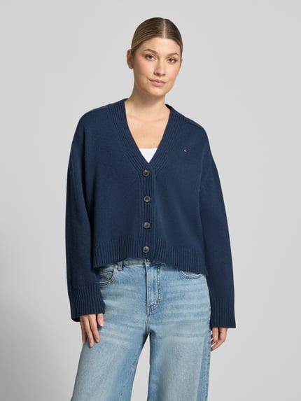 Frauenmodel trägt Cardigan aus Wolle mit Logo-Detail von Tommy Hilfiger in dunkelblauer Strickoptik, Knöpfe, Struktur, V-Ausschnitt, cropped, Ganzkörperansicht von vorne.