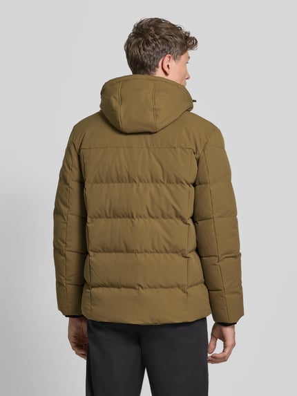 Männermodel trägt Steppjacke mit Kapuze von BRAX in Unifarbe mit Logo-Patch und Reißverschlusstaschen, Ganzkörperansicht Rückansicht.