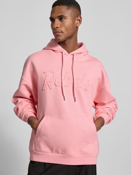 Männermodel trägt Hoodie mit Statement-Stitching von Dsquared2 in Rosa, reine Baumwolle, Relaxed Fit, Känguru-Tasche, Nahaufnahme Oberkörper.