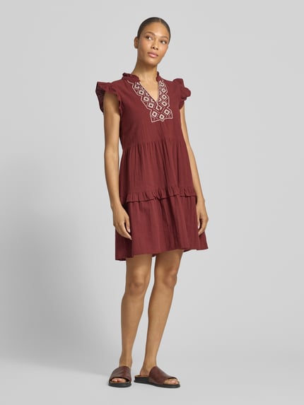 Frauenmodel trägt figurumspielendes Freizeitkleid aus reiner Baumwolle Modell 'Dichte' von Vero Moda, bordeaux, kurzarm, Mini-Länge, tiefer V-Ausschnitt, Struktur durch Flammgarn, unifarben, Ganzkörperansicht von vorne.