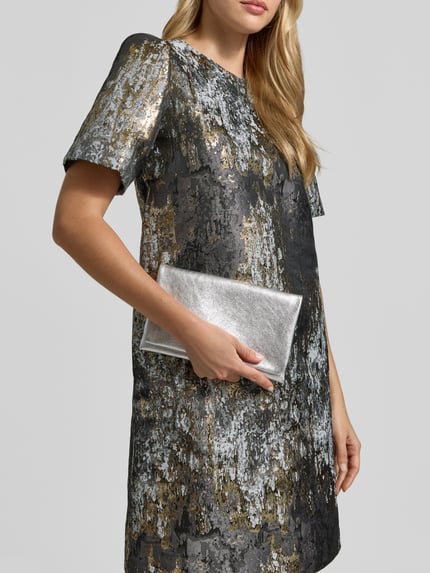 Frauenmodel trägt Clutch aus echtem Leder mit Strukturmuster von Abro in Silber, ergänzt Metallic-Kleid; Nahaufnahme Oberkörper. Hauptfach mit Umschlag und Magnetverschluss, Innenfach mit Reißverschluss, Label-Detail innen, Maße: 23x14x4 cm.