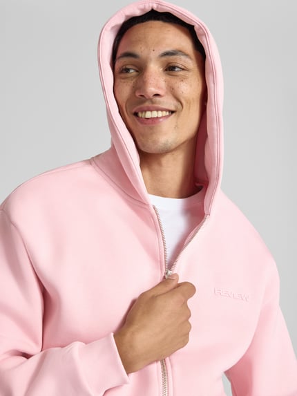 Männermodel trägt Sweatjacke aus Baumwoll-Mix von REVIEW in Rosa mit Reißverschluss und Kängurutasche, Nahaufnahme Oberkörper, lockere Passform, gerippte Abschlüsse