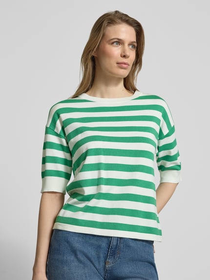 Modelka kobieca nosi zielono-biały damski t-shirt w paski z mieszanki wiskozy, krój regular fit, model 'Morla' od b.young, okrągły dekolt, rękaw o dł. 7/8, długość tyłu w rozmiarze S: 57 cm, długość rękawów: 23 cm, widok na górną część ciała z przodu.