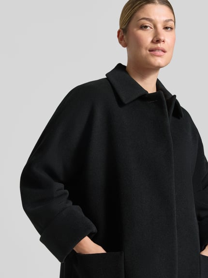 Frauenmodel trägt Mantel aus Lanawolle-Mix mit aufgesetzten Taschen von ICONS Cinzia Rocca, schwarze Struktur, Nahaufnahme Oberkörper.