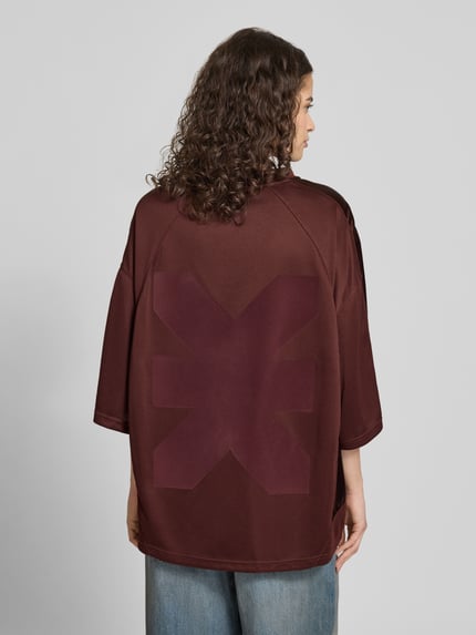 Frauenmodel trägt Oversized T-Shirt mit Label-Print von Karo Kauer, V-Ausschnitt, bordeaux, strukturierter Stoff, Rückansicht, Ganzkörperansicht.