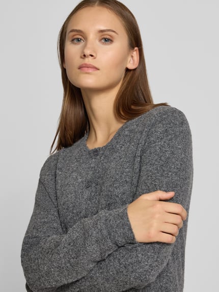 Frauenmodel trägt Regular Fit Strickjacke mit Lammwoll-Anteil von REVIEW, grau meliert, gerippte Abschlüsse, Knopfleiste, Langarm, Nahaufnahme Oberkörper.