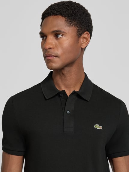 Männermodel trägt schwarzes Slim Fit Poloshirt aus reiner Baumwolle von Lacoste, glatte Struktur, Nahaufnahme Oberkörper.