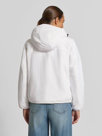 Frauenmodel trägt Regular Fit Jacke mit Logo-Print Modell 'CLAUDETTE' von K-WAY, Weiß, Kapuze, elastische Abschlüsse, Ganzkörperansicht Rückansicht. Kontext: Damen Jacke von K-WAY, Logo-Print, Regular Fit, Kapuze mit Tunnelzug, elastische Abschlüsse, Rückenlänge bei Größe S: 51 cm, Schulterbreite 41 cm, Brustweite 55 cm, Ärmellänge 61 cm.