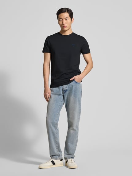Männermodel trägt T-Shirt mit Label-Detail von Gant in Schwarz, Reine Baumwolle, Gerader-Schnitt, Rundhalsausschnitt, Ganzkörperansicht von vorne. Rückenlänge bei Größe M: 70 cm.