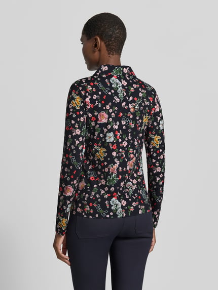 Männermodel trägt Slim Fit Hemdbluse mit floralem Allover-Print von Marc Cain, elastyczna mieszanka materiałów, kołnierzyk koszulowy, bluzka z długim rękawem, długość tyłu w rozmiarze 36: 59 cm, długość rękawów w rozmiarze 36: 63 cm, kwiatowe wzory na czarnym tle, widok całej sylwetki od tyłu.