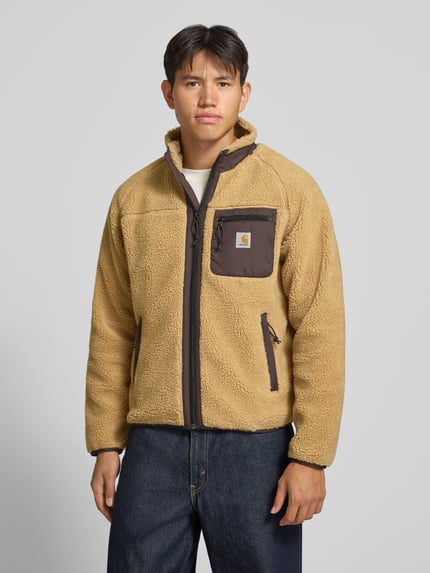 Männermodel trägt Teddyjacke mit Brusttasche Modell 'PRENTIS LINER' von Carhartt Work In Progress, beige, Reißverschlüsse, Ganzkörperansicht von vorne. Regular Fit, Stehkragen, Label-Patch, seitliche Reißverschlusstaschen, Rückenlänge 65 cm, Ärmellänge 51 cm.