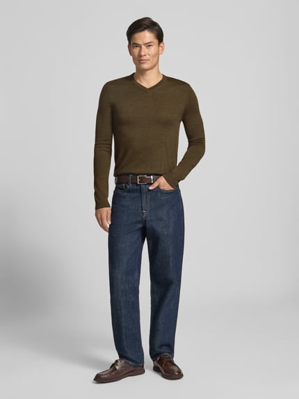 Männermodel trägt Strickpullover aus Woll-Mix mit V-Ausschnitt von Christian Berg Men in Oliv, dunkle Jeans, neutraler Hintergrund, Ganzkörperansicht von vorne. Regular Fit, gerippte Abschlüsse, Rückenlänge 71 cm, Ärmellänge 73 cm.