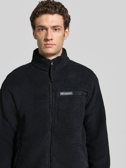 Männermodel trägt Regular Fit Fleecejacke mit Logo-Patch von Columbia, schwarze Farbe, Fleece, Nahaufnahme Oberkörper, Brusttasche sichtbar.