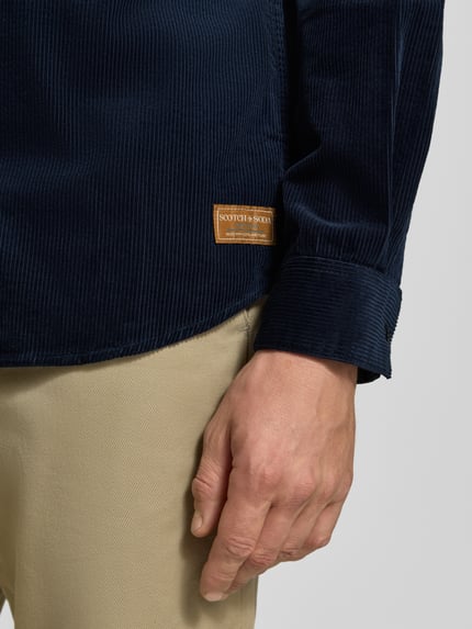 Männermodel trägt Regular Fit Cordhemd mit Brusttasche von Scotch & Soda, reine Baumwolle, Label-Patch, Nahaufnahme Unterarm.