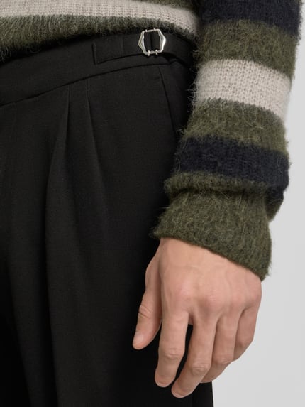 Männermodel trägt Regular Fit Bundfaltenhose mit Seitenriegel von MCNEAL, schwarze Struktur, Detailaufnahme, Kontext wie beschrieben.