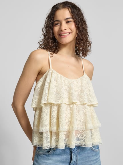 Frauenmodel trägt Regular Fit mit floralem Allover-Spitzenbesatz von Gina Tricot aus elastischem Material-Mix mit Rüschenbesatz und Spaghettiträgern, cremefarbene Spitze, Ganzkörperansicht von vorne.
