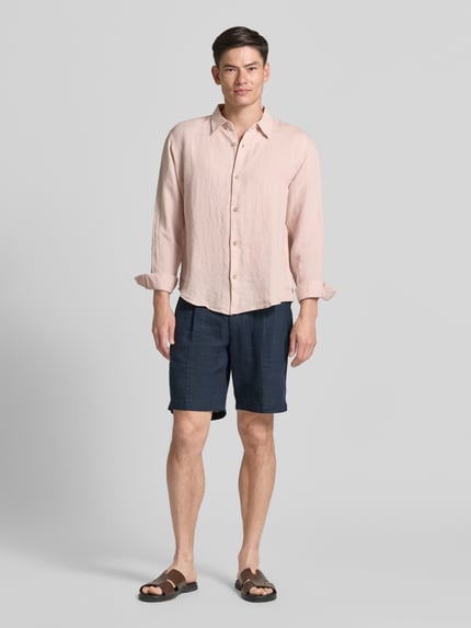 Männermodel trägt Regular Fit Leinenhemd mit Kentkragen von GAP in hellem Rosaton mit Knopfleiste, Regular-Fit, reine Leinenstruktur, Rückenlänge 71 cm, Schulterbreite 49 cm, Ärmellänge 64 cm, Ganzkörperansicht von vorne.
