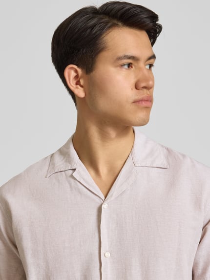 Männermodel trägt Regular Fit Freizeithemd aus Baumwoll-Leinen-Mix von Jack & Jones in Beige mit Reverskragen, Knopfleiste, Nahaufnahme Oberkörper.