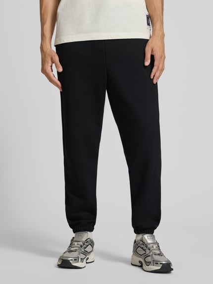 Männermodel trägt Sweatpants mit Label-Print von Alpha Industries, Mieszanka bawełny, luźny krój, Elastyczny pas z tunelem, wpuszczane kieszenie, nadruk z logo, Długość wewnętrzna nogawki w rozmiarze M: 44 cm, Ganzkörperansicht von vorne