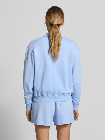 Modelka kobieca nosi Regular Fit Sweatshirt aus Baumwoll-Mix od Polo Ralph Lauren, jasnoniebieski, bawełniany, gładka tekstura, krój regular fit, logo, polokragni z dekoltem V, zapięcie na dwa guziki, długie rękawy, ściągacze na rękawach i dole, widok całej sylwetki z tyłu.