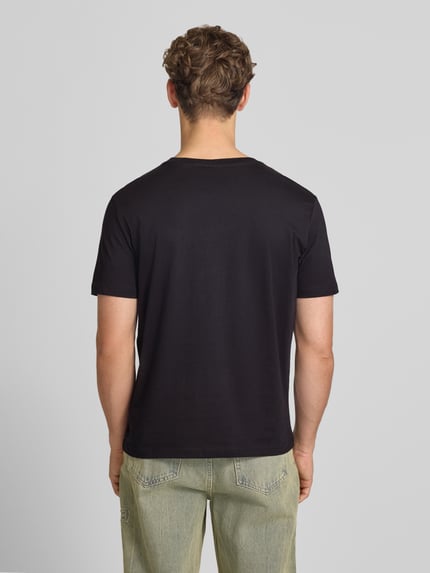 Männermodel trägt T-Shirt mit Label-Stitching mit Rundhalsausschnitt von CHAMPION aus Reine Baumwolle, Regular-Fit, Rückenlänge 68 cm, Ganzkörperansicht Rückansicht.