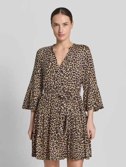 Frauenmodel trägt Tailliertes Tunikakleid aus reiner Viskose Modell 'MELBA' von Vero Moda mit Allover-Leopardenmuster, V-Ausschnitt, Trompetenärmeln, Bindegürtel, Volantsaum, Mini-Länge, beige und schwarz, Ganzkörperansicht von vorne