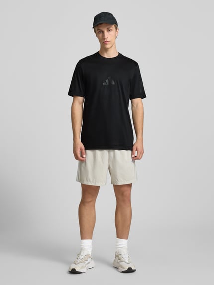 Männermodel trägt Regular Fit T-Shirt aus reiner Baumwolle von adidas Sportswear in Optik: Unifarben, Logo-Print, Rundhals, Kurzarm, Ganzkörperansicht von vorne.