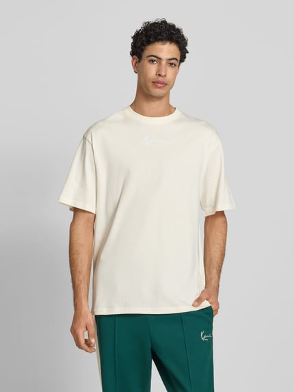 Männermodel trägt T-Shirt mit Label-Stitching und Rundhalsausschnitt von KARL KANI, Herren T-Shirt aus Reine Baumwolle, Relaxed-Fit, Frontansicht, Rückenlänge bei Größe M 70 cm.