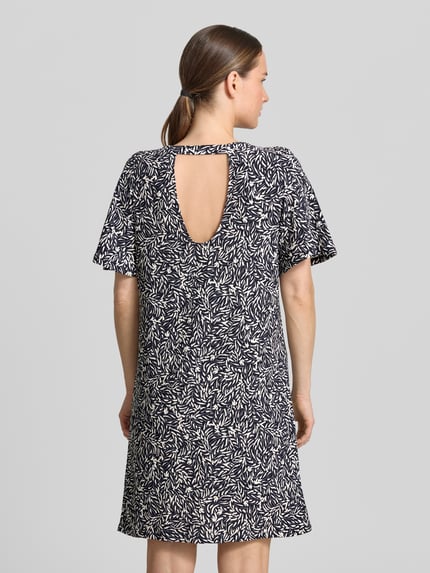Modelka kobieca nosi 'Knielanges Kleid im Allover-Look' od Zero, czarno-białe liściaste wzory, prosty krój, okrągły dekolt, materiał z domieszką stretchu, długość do kolan, szerokość w rozmiarze 36: 48 cm, długość tyłu: 90 cm, długość rękawa: 30 cm, widok całej sylwetki z tyłu.