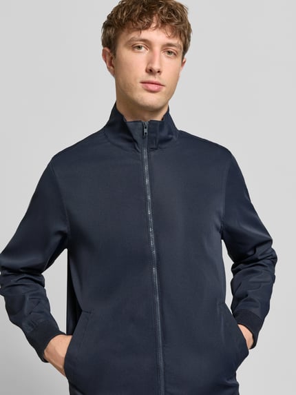 Männermodel trägt Regular Fit Jacke mit Stehkragen Modell 'Hefi' von Blend in Dunkelblau, Reine Baumwolle, Nahaufnahme Oberkörper. Rückenlänge 71 cm, Schulterbreite 46 cm, Brustweite 48 cm, Ärmellänge 25 cm, Reißverschluss, Eingrifftaschen, elastische Abschlüsse.