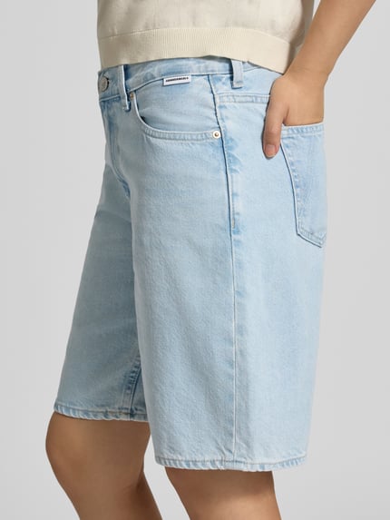 Frauenmodel trägt hellblaue Regular Fit Jeansshorts aus reiner Baumwolle Modell 'THALINAA' von Armedangels, Damen Jeansshorts, Nahaufnahme Oberschenkel.