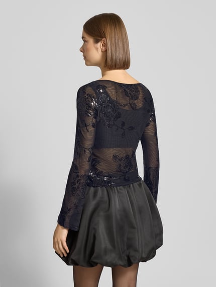 Frauenmodel trägt Slim Fit Longsleeve mit floralem Pailettenbesatz von Gina Tricot, semitransparent, schwarz, ausgestellte Ärmel, Ganzkörperansicht Rückansicht.