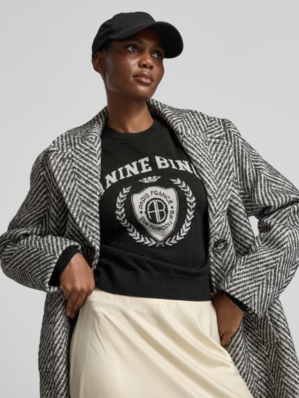 Frauenmodel trägt Sweatshirt mit Logo-Front Modell 'MIA SWEATER' von Anine Bing, melange Optik, Motiv-Print, Feinstrick, Nahaufnahme Oberkörper.