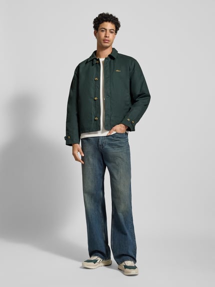 Męski model nosi Jacke mit Label-Stitching und Eingrifftaschen od BLKVIS, ciemnozielony kolor, regular fit, pełen przód, widok całej sylwetki.