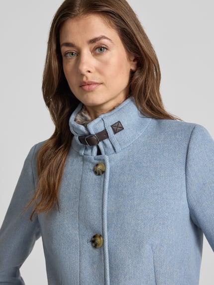 Frauenmodel trägt Mantel mit Kunstfell und Pattentaschen von Christian Berg Woman Selection in Hellblau, Material-Mix mit Woll-Anteil, Nahaufnahme Oberkörper.