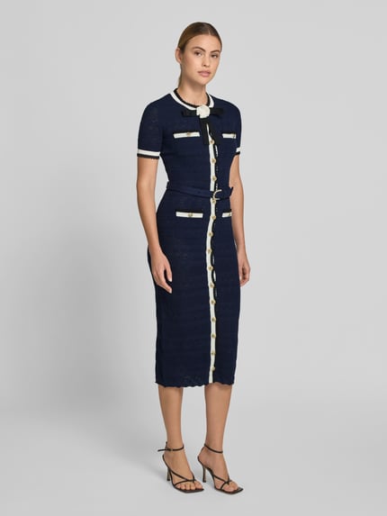 Modelka nosi Slim Fit Midikleid in Strick-Optik von Self-Portrait, granatowy kolor, imitacja dzianiny, krój slim fit, mieszanka bawełny elastycznej, listwa guzikowa na całej długości, z krótkim rękawem, całkowita długość w rozmiarze S: 126 cm, szerokość klatki piersiowej w rozmiarze S: 41 cm, długość rękawów w rozmiarze S: 23 cm, szerokość w talii w rozmiarze S: 34 cm, widok całej sylwetki z przodu