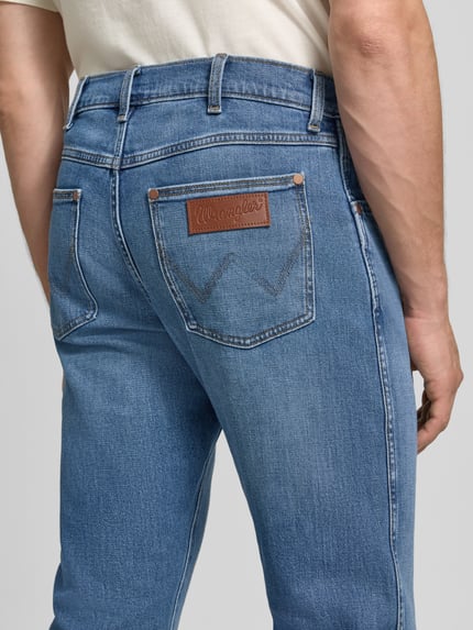Männermodel trägt Regular Taper Jeans aus Baumwoll-Mix Modell 'Redford' von Wrangler, hellblaue Farbe, robuste Textur, Ganzkörperansicht Rückansicht, Herren Taper Jeans von Wrangler.