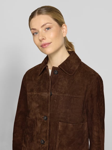 Frauenmodel trägt Lederjacke aus Ziegenvelours mit Eingrifftaschen von Christian Berg Woman, braune Farbe, glatte Textur, Nahaufnahme Oberkörper.