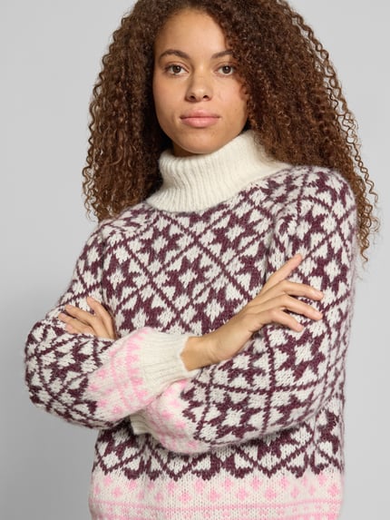 Frauenmodel trägt Rollkragenpullover mit Ballonärmeln von ONLY in Jacquard-Strick, mehrfarbige Rauten und Sternenmuster, Nahaufnahme Oberkörper.