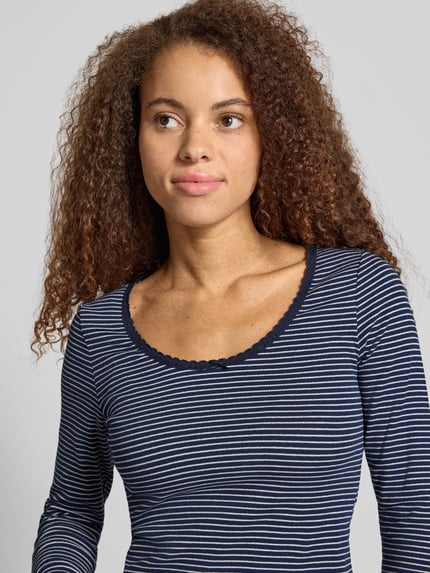 Frauenmodel trägt T-Shirt mit Rippstrickstruktur von LEVIS 300, gestreiftes Allover-Muster, U-Ausschnitt, Langarm, Nahaufnahme Oberkörper.