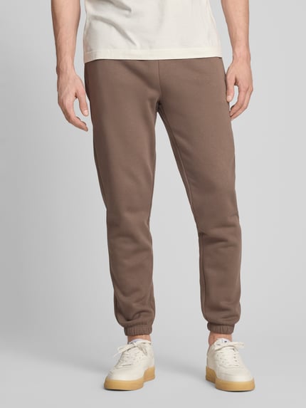 Männermodel trägt Sweatpants mit Eingrifftaschen von GAP aus Baumwoll-Mix, Regular-Fit, Logo, braun, Ganzkörperansicht von vorne.