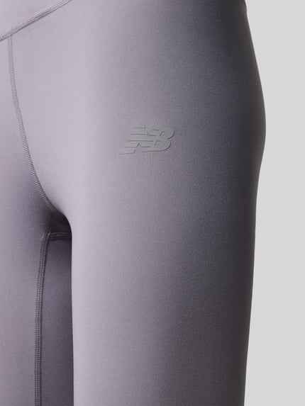 Frauenmodel trägt Slim Fit Leggings mit Logo-Print Modell 'Harmony' von New Balance, grauer Jersey-Stoff, Nahaufnahme Oberschenkel.