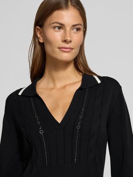 Frauenmodel trägt Knielanges Strickkleid mit Kontraststreifen von Liu Jo, Schwarz mit Zopfmuster und Strasssteinbesatz, Nahaufnahme Oberkörper. Damen Strickkleid von Liu Jo Sport, Viskose-Mix, taillierter Schnitt, V-Ausschnitt, Polokragen, Kontraststreifen.