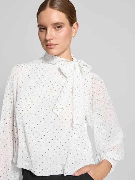 Frauenmodel trägt Schluppenbluse mit elastischen Ärmelabschlüssen Modell 'Dorellie' von Neo Noir, weiß mit kleinen schwarzen Punkten, Regular Fit, Nahaufnahme Oberkörper.