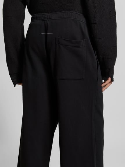 Männermodel trägt Wide Fit stoffen broek met achterzak van MM6 Maison Margiela in zwart, puur katoen, elastische band, detailaufnahme rug.