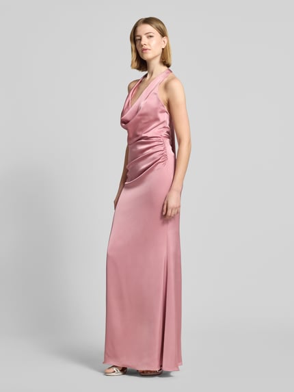 Modelka damska ma na sobie 'Abendkleid mit tiefem Rückenausschnitt und Neckholder' od Mascara, satynowy materiał, kolor różowy, krój slim fit, długość maxi, dekolt wodospadowy, zapięcie na szyi na haczyk, marszczenia, tylny zamek i głęboki dekolt z tyłu, długość pleców w rozmiarze 36: 136 cm, szerokość w rozmiarze 36: 41 cm, widok całej sylwetki z przodu.
