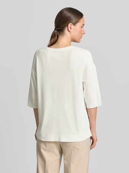 Frauenmodel trägt Damen T-Shirt mit Ärmelaufschlag und Rundhalsausschnitt von Marc Cain, Baumwoll-Mix mit Stretch-Anteil, Straight Fit, Label-Detail, Rückenlänge bei Größe 36: 62 cm, einfarbig hell, glatte Struktur, Ganzkörperansicht Rückansicht.