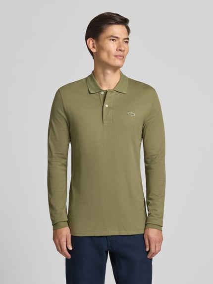Männermodel trägt Regular Fit Poloshirt aus reiner Baumwolle von Lacoste in Olivgrün, glatte Oberfläche, Ganzkörperansicht von vorne. Herren Poloshirt von Lacoste