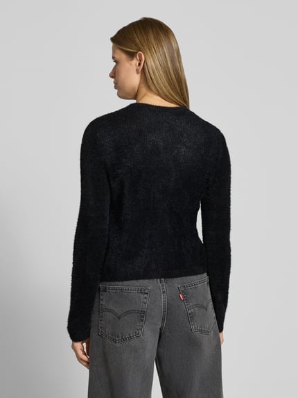 Frauenmodel trägt Strickjacke mit Herzknöpfen von ONLY in Schwarz auf grauer Jeans, weiche Textur, Ganzkörperansicht Rückansicht.